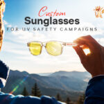 Custom sunglasses held against sunlight, illustrating their use in UV Safety Awareness Month campaigns and outdoor sun protection.