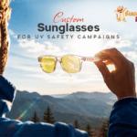 Custom sunglasses held against sunlight, illustrating their use in UV Safety Awareness Month campaigns and outdoor sun protection.