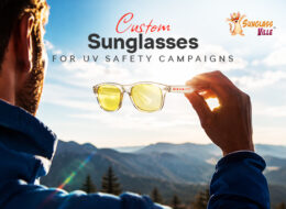 Custom sunglasses held against sunlight, illustrating their use in UV Safety Awareness Month campaigns and outdoor sun protection.