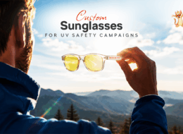 Custom sunglasses held against sunlight, illustrating their use in UV Safety Awareness Month campaigns and outdoor sun protection.